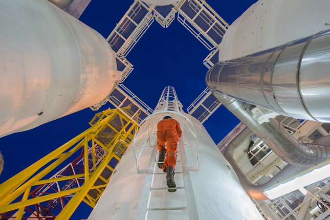 A power plant worker climbing ladder to the top of a giant metal chimney.